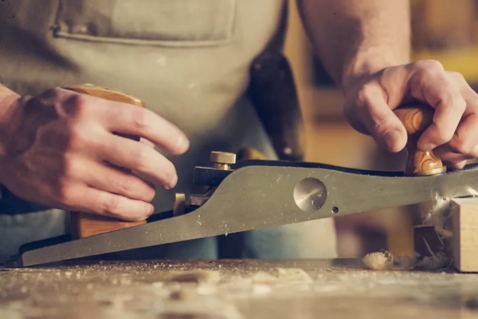 Mains rabotant une pièce de bois en atelier.